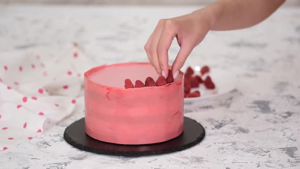 Woman hands placing a raspberries onto freshly cooked cake.	