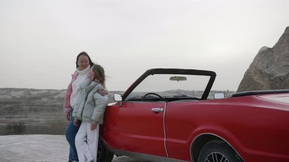 Mom and Daughter Standing Near Retro Cabriolet Red Car in Rocks Admiring View