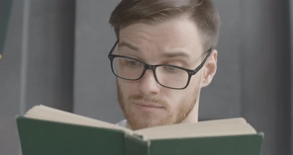 Close-up Face of Smart Young Man in Eyeglasses Reading Book alt