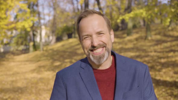 A Middleaged Caucasian Man Laughs at the Camera in a Park in Fall  Closeup