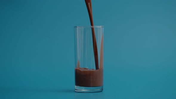 Super Slow Motion of Pouring Chocolate Milk in Transparent Glass Blue Background alt