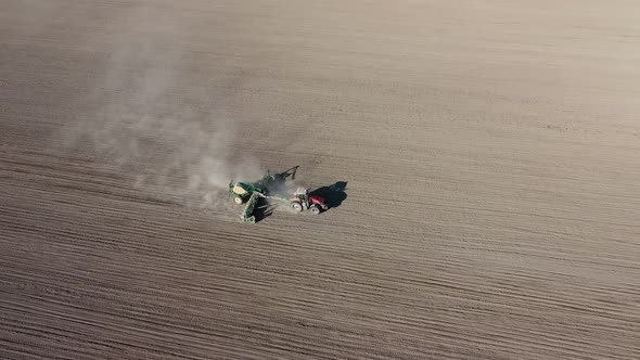 Aerial view of tractor with harrow system plowing ground on cultivated farm field alt