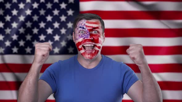 A screaming American cheerleader with a face painted in the color of the US flag.