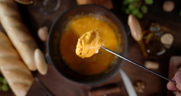 Male Hand Dips a Piece of Bread in Fondue. On Wooden Background. alt