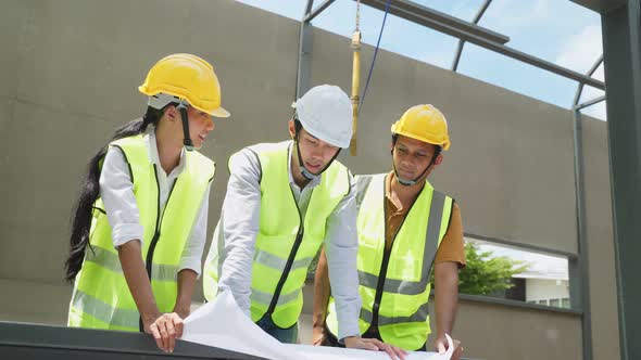 Asian colleague workers people wearing safety helmet, holding drawing working on construction. alt