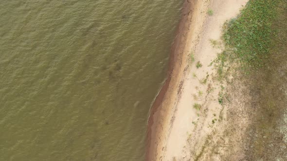 AERIAL: Rotating Shot of Coast with Grass Growing on Sand and Rippling Water 
