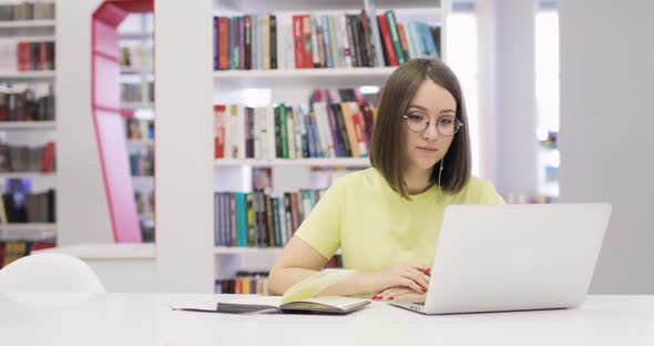 Young Woman is Smiling Sitting at a Desk with a Laptop Working in the Library
