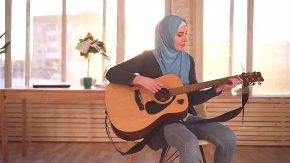 Young Muslim Woman Musician in Hijab Playing Guitar in Modern Apartment alt