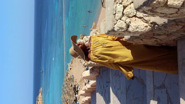 Happy African American Woman in Yellow Dress and Sun Hat Enjoys View of Coast of Red Sea on Natural