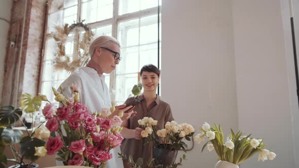 Middle Aged Woman Using Tablet and Speaking with Young Female Florist alt