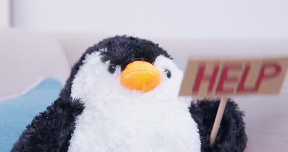 A Stuffed Penguin Toy Sitting on the Sofa Raises a Help Sign