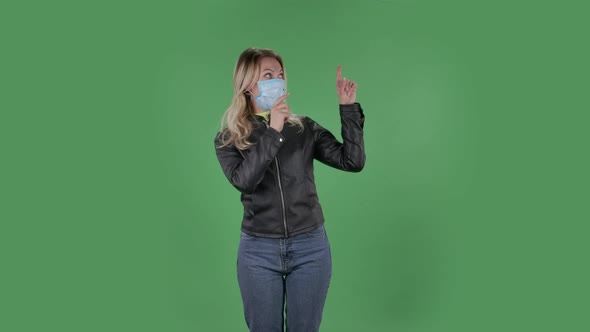 Portrait of Beautiful Young Woman in Medical Protective Face Mask Looking at Camera and Pointing alt
