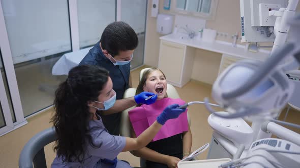 Professional Dentist Using Tooth Dryer and Mouth Mirror Examining Patient with Help of Assistant alt