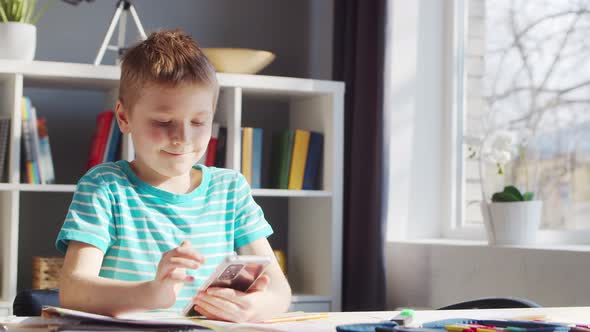 Boy is Doing  Homework at the Table. Cute Child is Learning at Home. alt