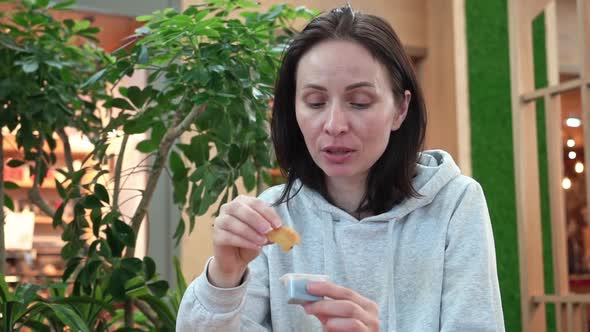 Young Beautiful Brunette Woman of European Appearance Sits in a Cafe in a Shopping Center and Eats alt