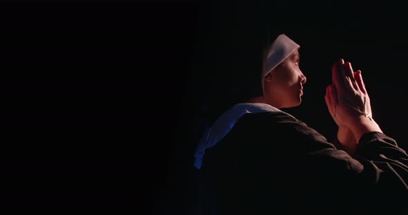 Nun Praying In The Dark While Kneeling