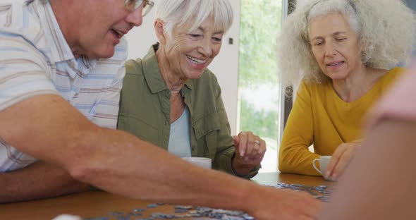 Happy senior diverse people playing puzzle at table at retirement home alt