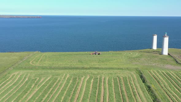 Tracking aerial dolly of red tractor in green field before blue ocean alt