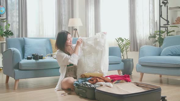 Asian Young Woman Looking At Shirt And Packing Clothes In Suitcase At Home, Preparing For Vacation alt