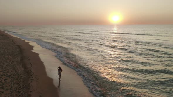 Beautiful Scene of a Woman Walking on Ocean Beach at Sunset alt