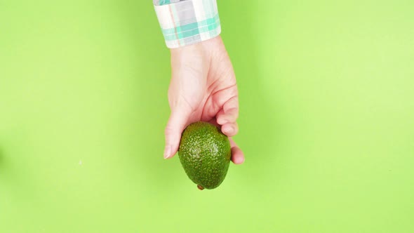 Female hand in a plaid shirt holds ripe juicy avocado hass on a green background