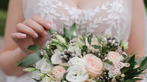 A young bride in a white dress examines and touches the wedding bouquet. Steadicam close-up shot alt