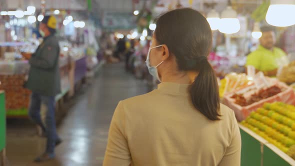 Asian woman wearing protective face mask walking at fresh market.