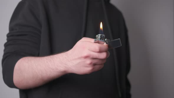 A guy in a black tracksuit lights a gasoline metal lighter and then extinguishes