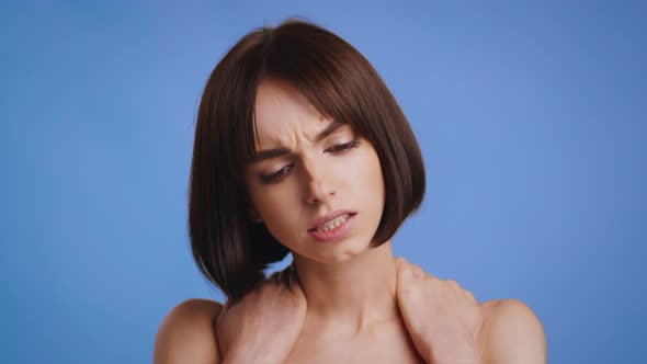 Young Woman Massaging Aching Neck Standing On Blue Studio Background alt
