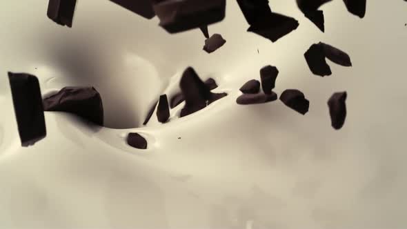 Various size of chocolates pieces fall down into pouring creamy milk in slow motion