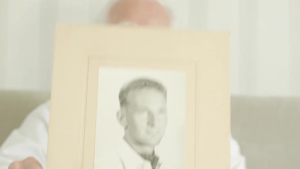 Senior Man Holding up a Photo of Himself as a Young Man