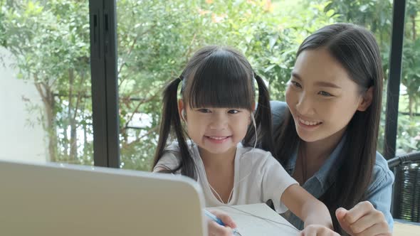 Young Asian dad enjoys teaching his lovely daughter do a homework on a laptop.