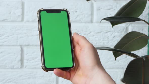 Man Using Smart Phone in Office Space Sitting on Chair and Using Green Screen Phone Mockup Chroma