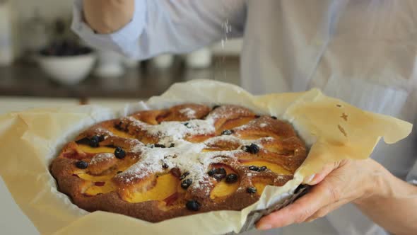 Close-up of senior woman sprinkling freshly baked tart with powdered sugar alt