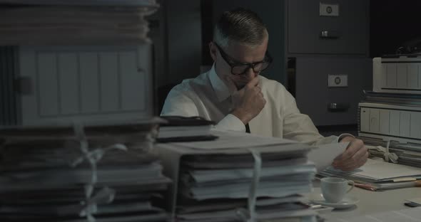 Disappointed businessman working overtime in the office, he is checking paperwork