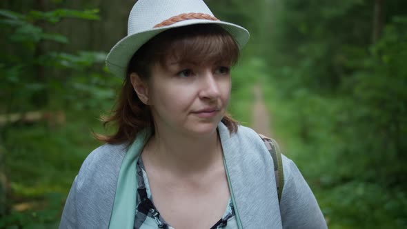 Woman in a Hat and with a Backpack Walks Through the Forest Close Up