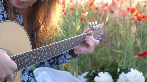 Young woman playing guitar at sunset in a field of flowers in summer. People, relaxation, lifestyle.