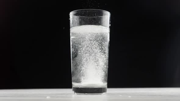 Effervescent aspirin tablet dropping to glass of water. alt