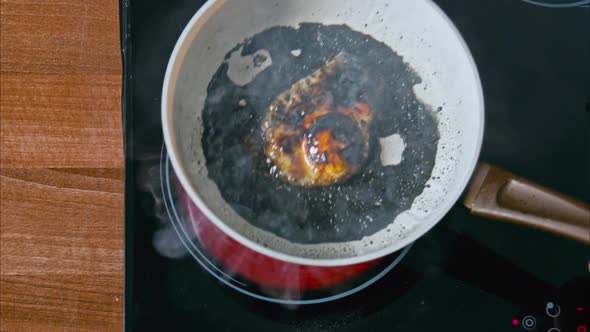 Burnt Egg on a White Pan in Black Oil on a Black Stove