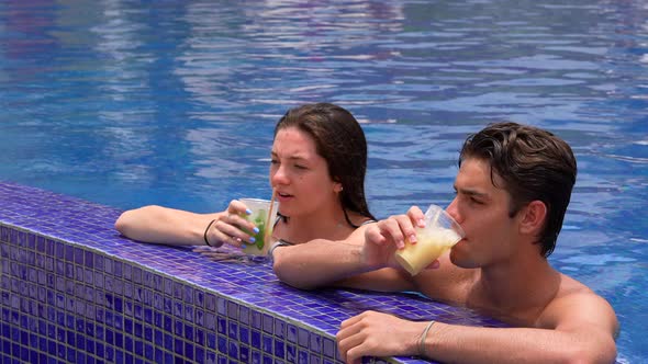 Underage teen couple drinking cocktails in pool at all-inclusive resort honeymoon destination. alt