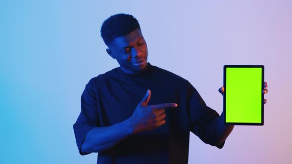 Black Man Holding a Digital Tablet with a Green Screen Pointing at the Tablet alt
