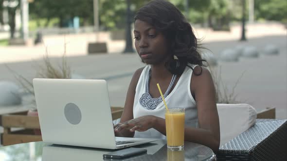 African American Woman Working on Laptop Outdoor and Drinking Juce alt