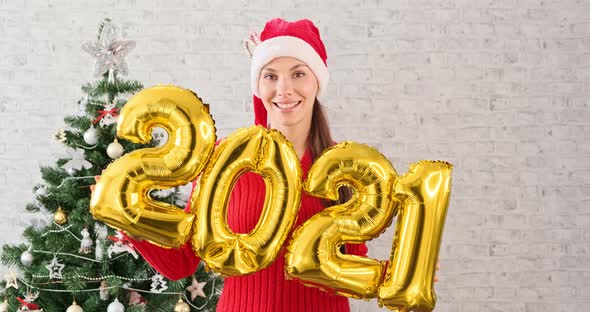 Young Woman in Santa Claus Hat Dancing and Having Fun Holding in Hand Numbers 2021. Girl in alt