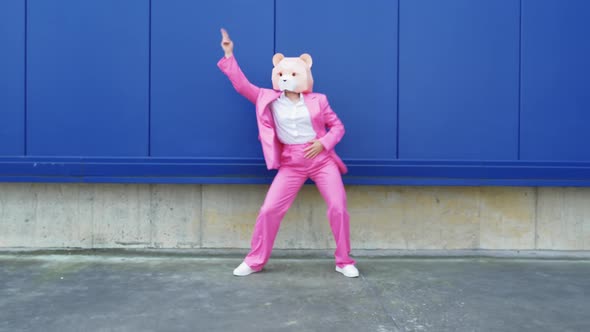 Woman in pink business suit and bear mask dancing in front of wall
