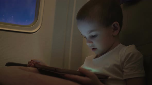 Cute Boy Traveling in an Airplane and Playing with a Computer Tablet alt