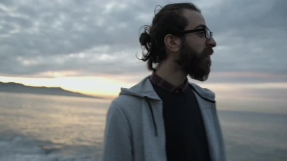 Young male with bulk haired beard and glasses walks along the seaside