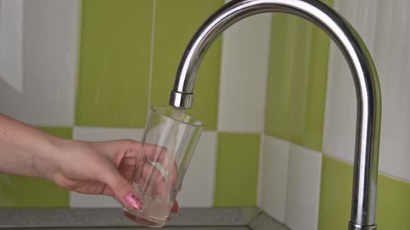 Women's Hands Collect Running Water From the Tap Into a Glass of Slowmo alt