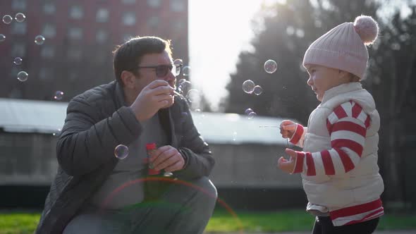 Caucasian Man with His Child Blowing Soap Bubbles Outside. Slow Motion. Weekend Activity alt