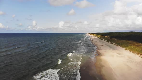 AERIAL: Flying backwards on a bright day over sandy Baltic Sea beach alt