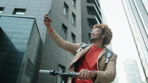 Positive Afro Man Standing in City with E-Scooter and Taking Selfie alt
